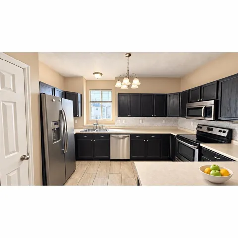 Kitchen featuring dark-finish cabinetry, stainless steel appliances, light-toned countertops, and tile flooring