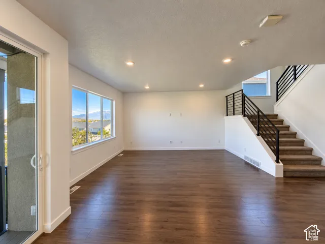 Spacious room featuring wood-finish flooring, recessed lighting, large windows, and a staircase with metal railings
