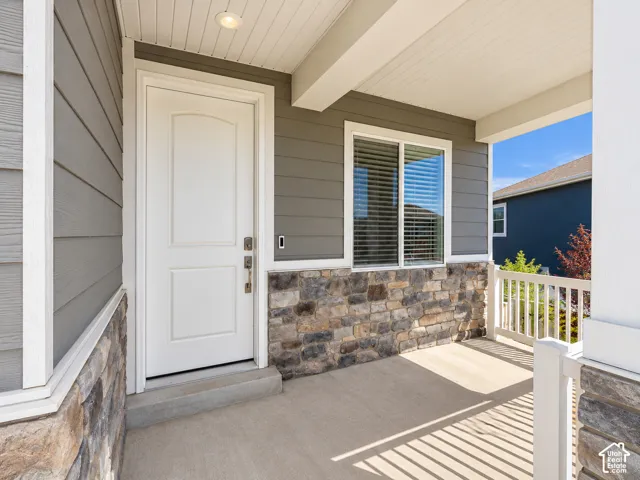 Covered front porch featuring stone veneer accents, durable siding, a white entry door, and a single window with blinds