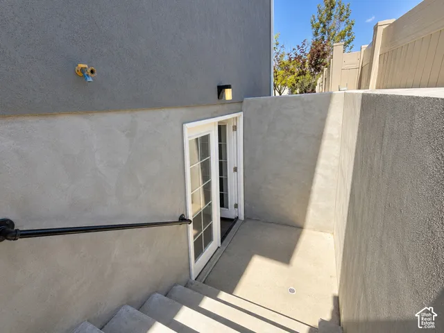 Exterior access featuring concrete stairs, a black metal handrail, white French doors, and stucco walls