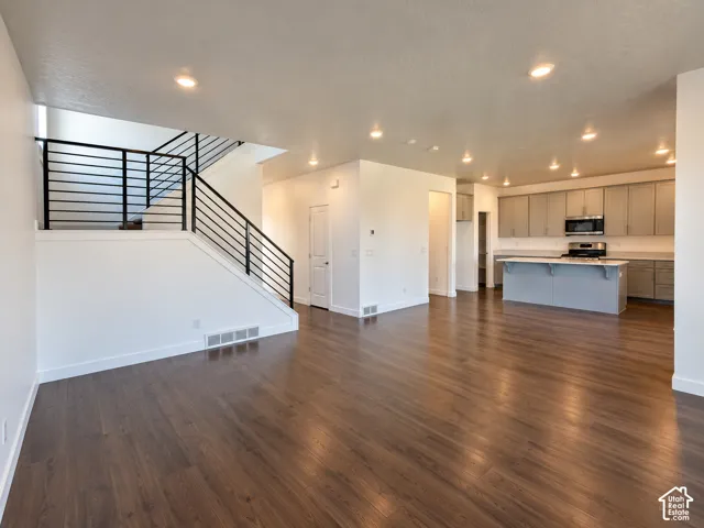 Open-concept living space featuring wood-finish flooring, a modern staircase with black horizontal railings, recessed lighting, and a kitchen with grey cabinetry and an island