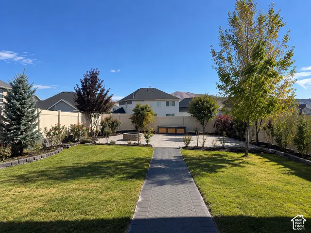 Expansive backyard featuring a paver patio with a built-in fire pit, a herringbone paver pathway, mature trees, and a privacy fence