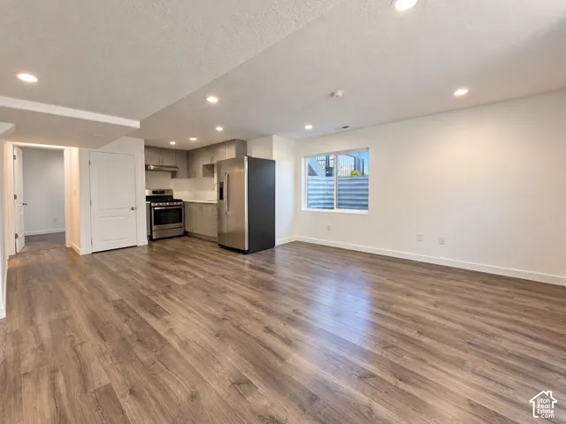 Open-concept living area featuring wood-finish flooring, recessed lighting, and a kitchen with stainless steel appliances, shaker-style cabinetry, and light countertops