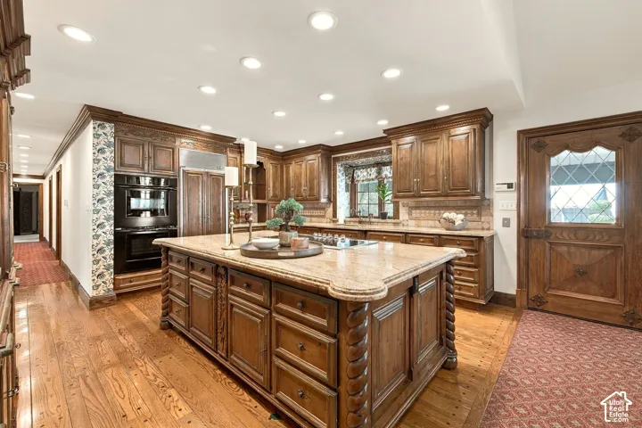 Spacious kitchen featuring wood-finish flooring, recessed lighting, built-in double ovens, a built-in refrigerator, and a large center island with a stone countertop