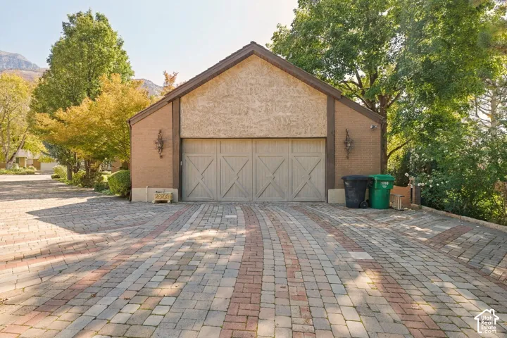 Gabled facade with stucco and brick accents, flanked by decorative exterior lighting, and a multi-tone paver driveway
