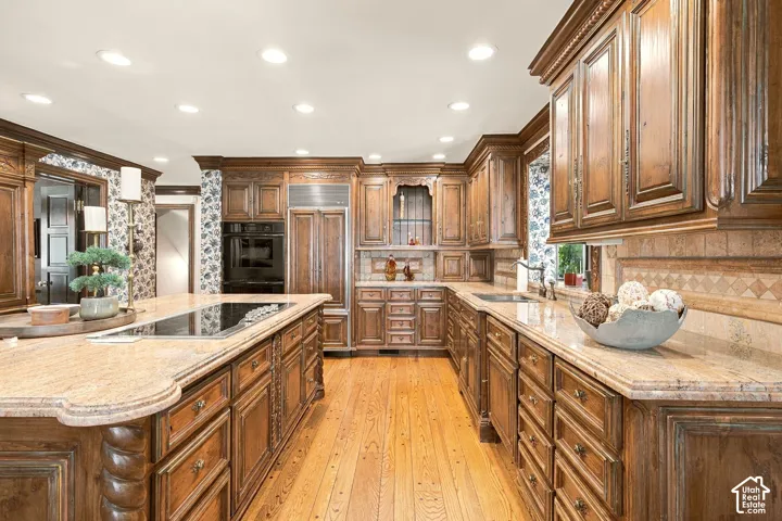Custom cabinetry with carved details and ornate hardware, light-toned countertops, hardwood flooring, built-in cooktop, and integrated stainless steel appliances
