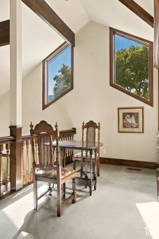 Vaulted ceiling featuring exposed wood beams, angular windows with wood trim, and a wood-finished railing