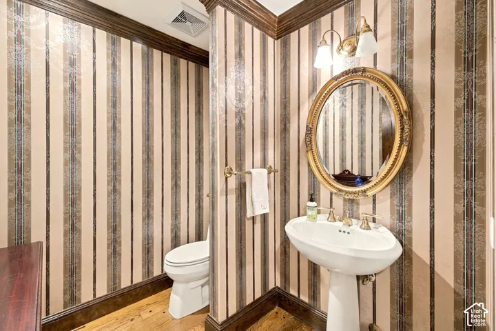 Pedestal sink with brass-finish faucet, ornate gold-frame oval mirror, and wall-mounted vanity lighting