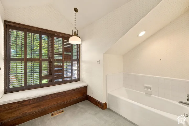 Built-in window seat with wood-finish paneling, full-height shutters, recessed lighting, and a drop-in bathtub with tiled surround