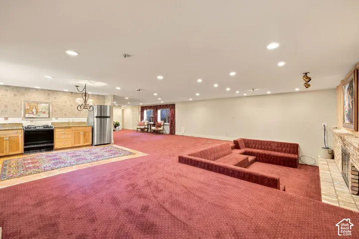 Expansive room featuring recessed lighting, a built-in kitchen area with wood cabinetry and a stainless steel refrigerator, and a multi-tiered built-in seating area