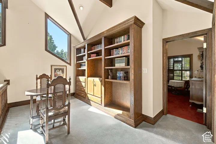 Vaulted ceiling with exposed wood beams, custom built-in wood shelving with cabinetry, and a large angled window