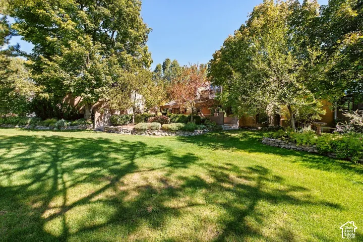 Expansive manicured lawn with mature trees, stone retaining walls, and planted garden beds