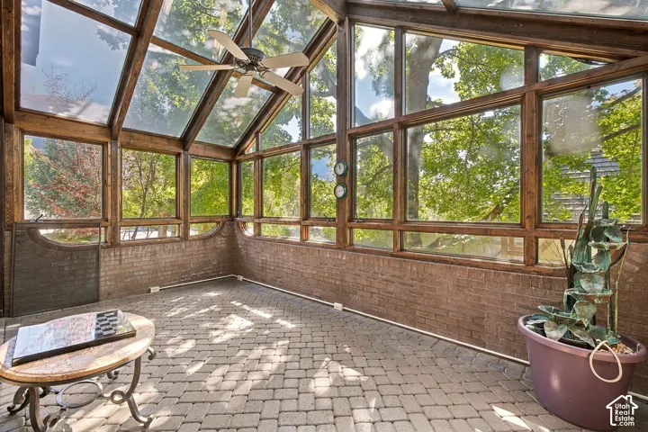 Sunroom featuring an exposed brick half-wall, extensive wood-framed windows, a vaulted glass ceiling, and paver flooring