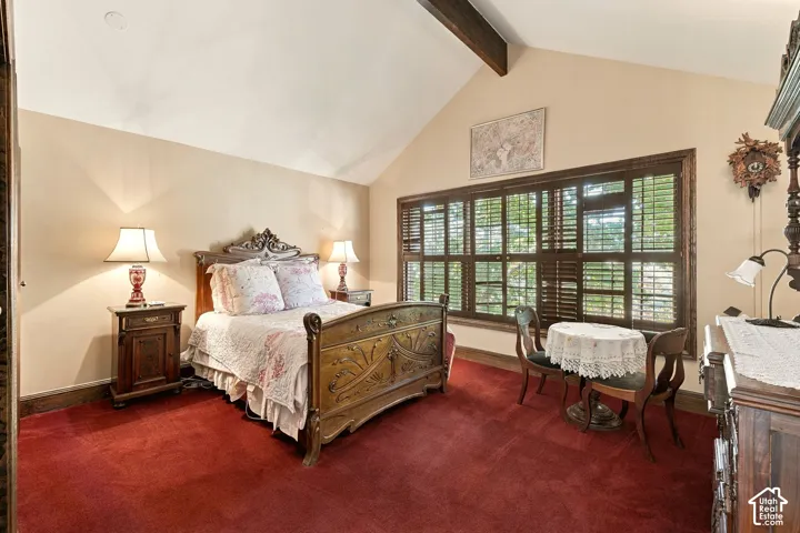 Vaulted ceiling with exposed wood beam, large window with wood plantation shutters, red carpeting, and light-toned walls