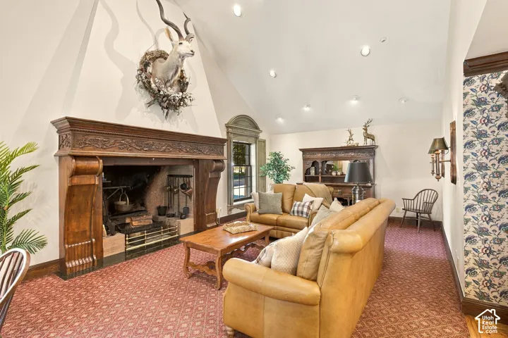 Vaulted ceiling with recessed lighting, large carved wood fireplace, patterned carpeting, decorative wall sconce, and built-in wood cabinetry