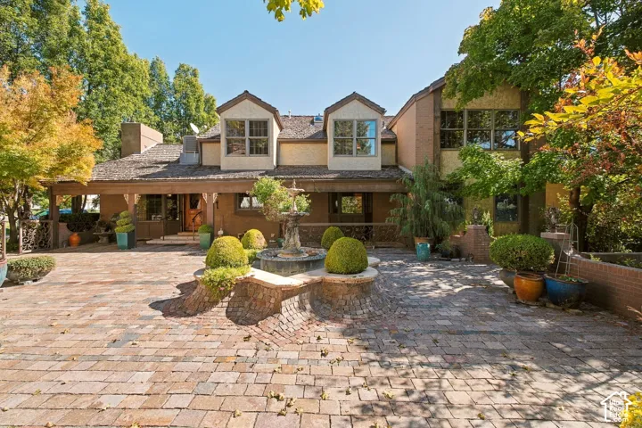 Brick paver driveway with a central tiered fountain, covered front porch, and dormer windows