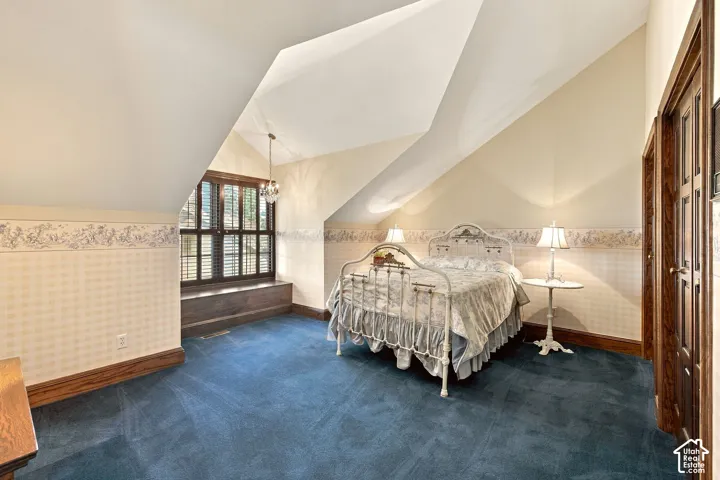 Vaulted ceiling with angled walls, dark wood-finish window shutters, blue carpet flooring, and a crystal pendant light fixture