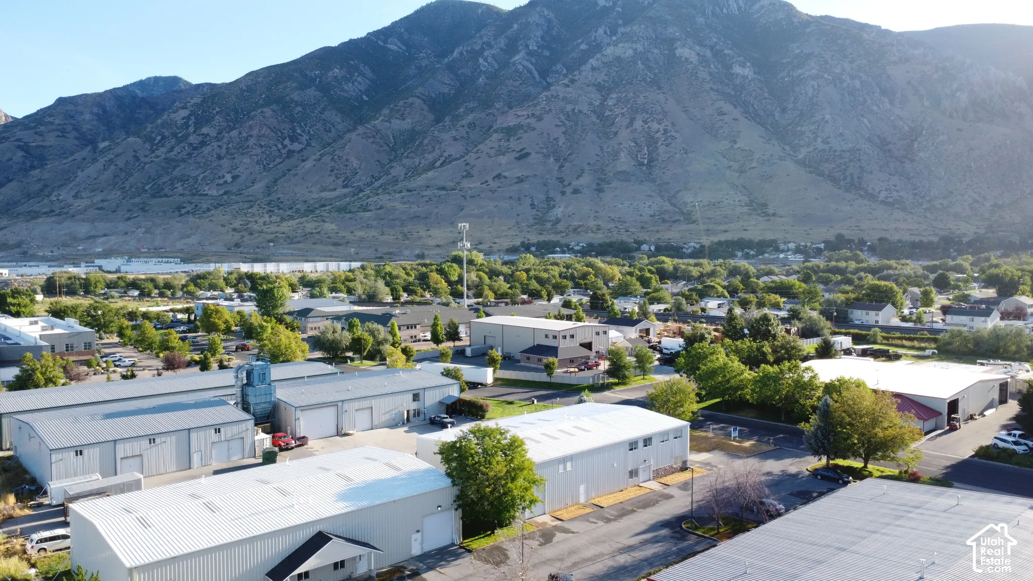 Multiple industrial-style buildings with metal siding and roofs, set within a developed area featuring mature trees