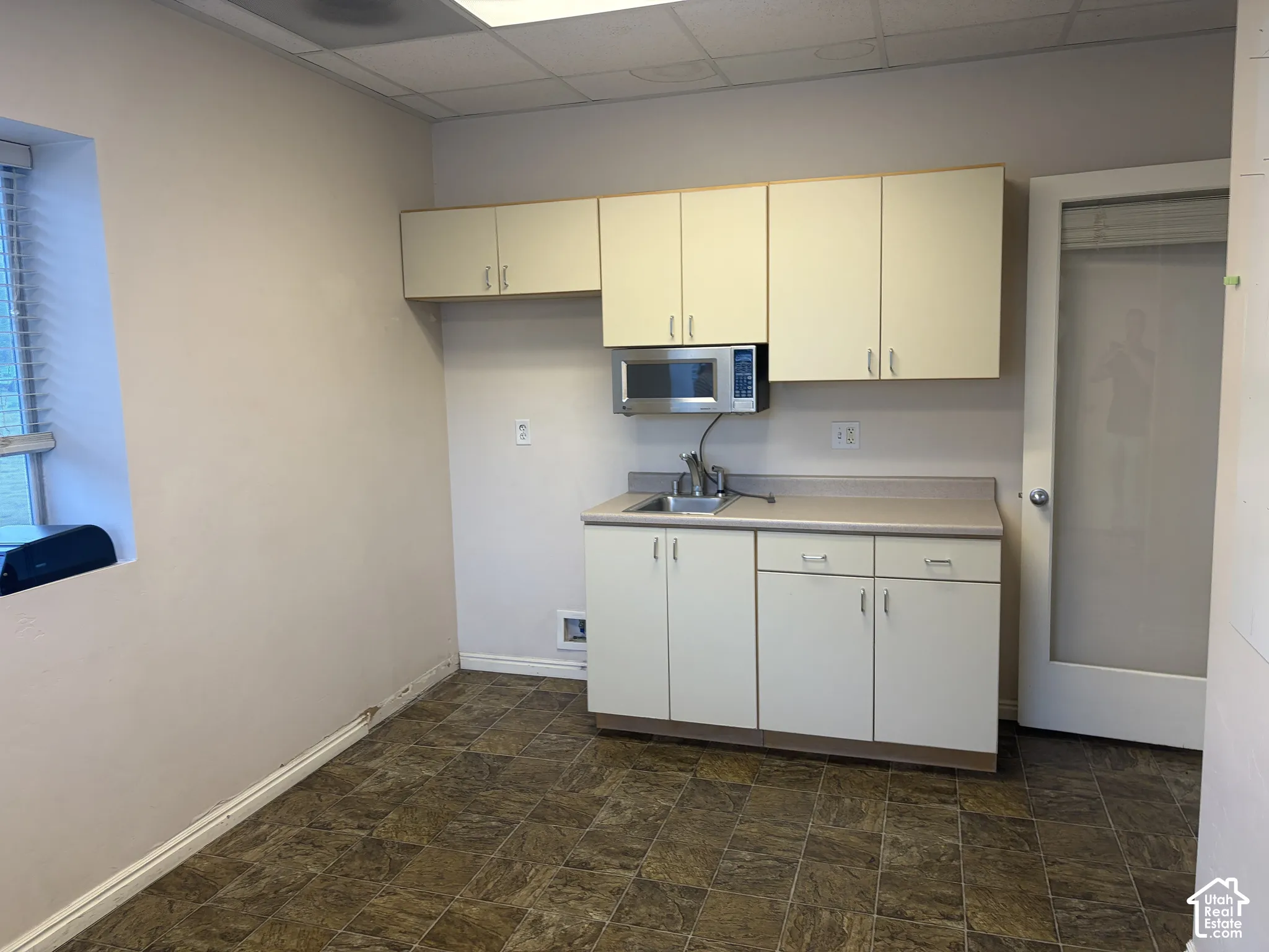 Compact kitchen area featuring a stainless steel microwave, single basin sink, and ample cabinetry