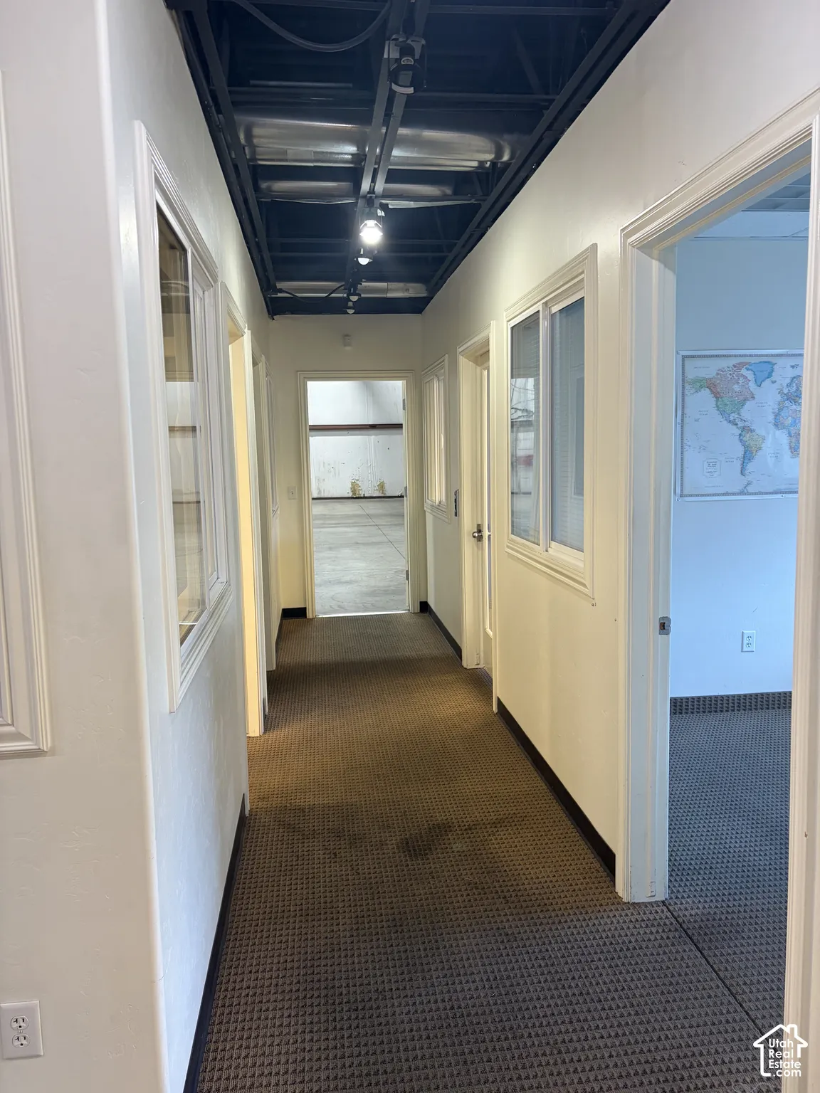 Corridor featuring textured carpet flooring, white walls, multiple doorways, and an exposed ceiling with track lighting