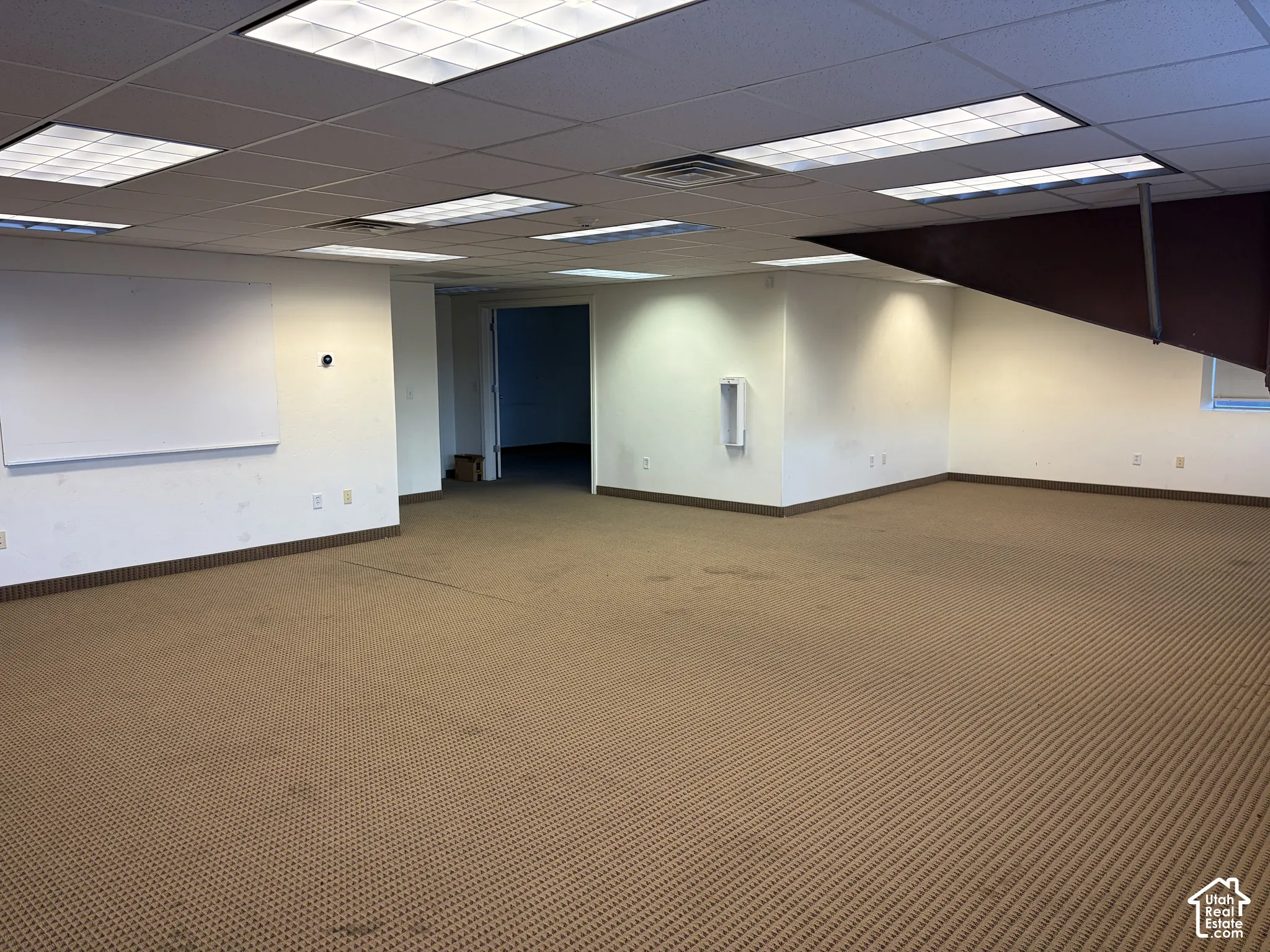 Recessed fluorescent lighting, drop ceiling, textured carpet flooring, and a built-in whiteboard