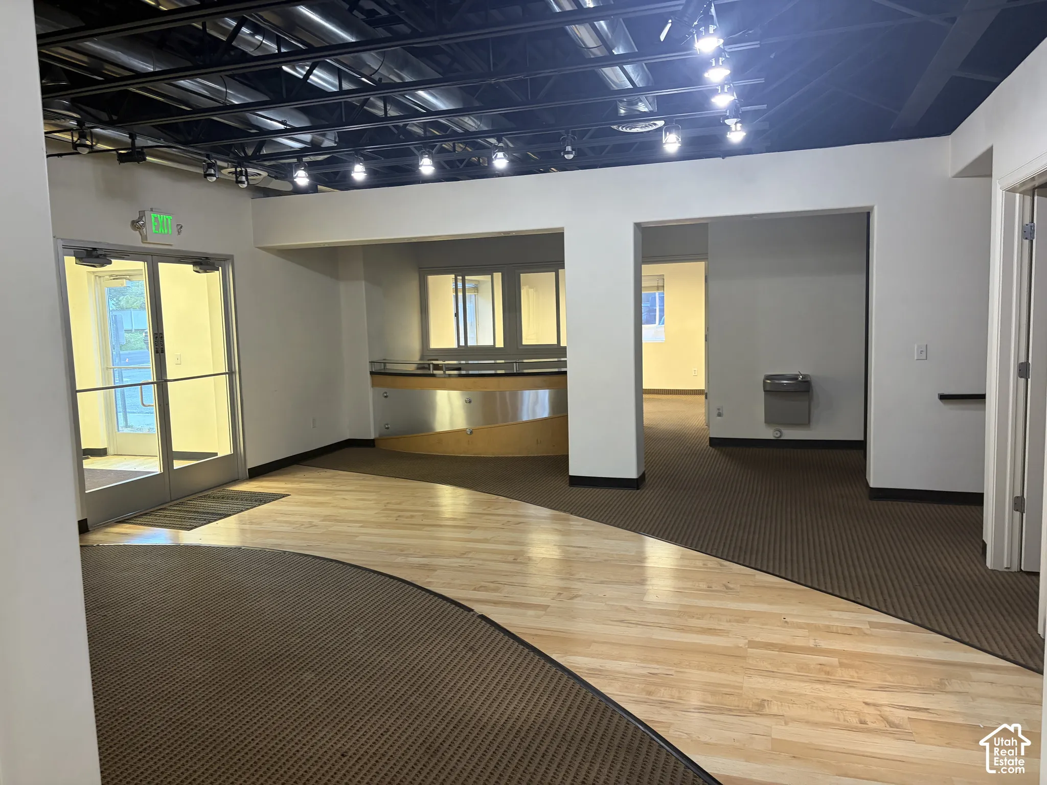 Exposed ceiling with track lighting, glass entry doors, built-in reception desk, wood-finish flooring, and wall-mounted water fountain