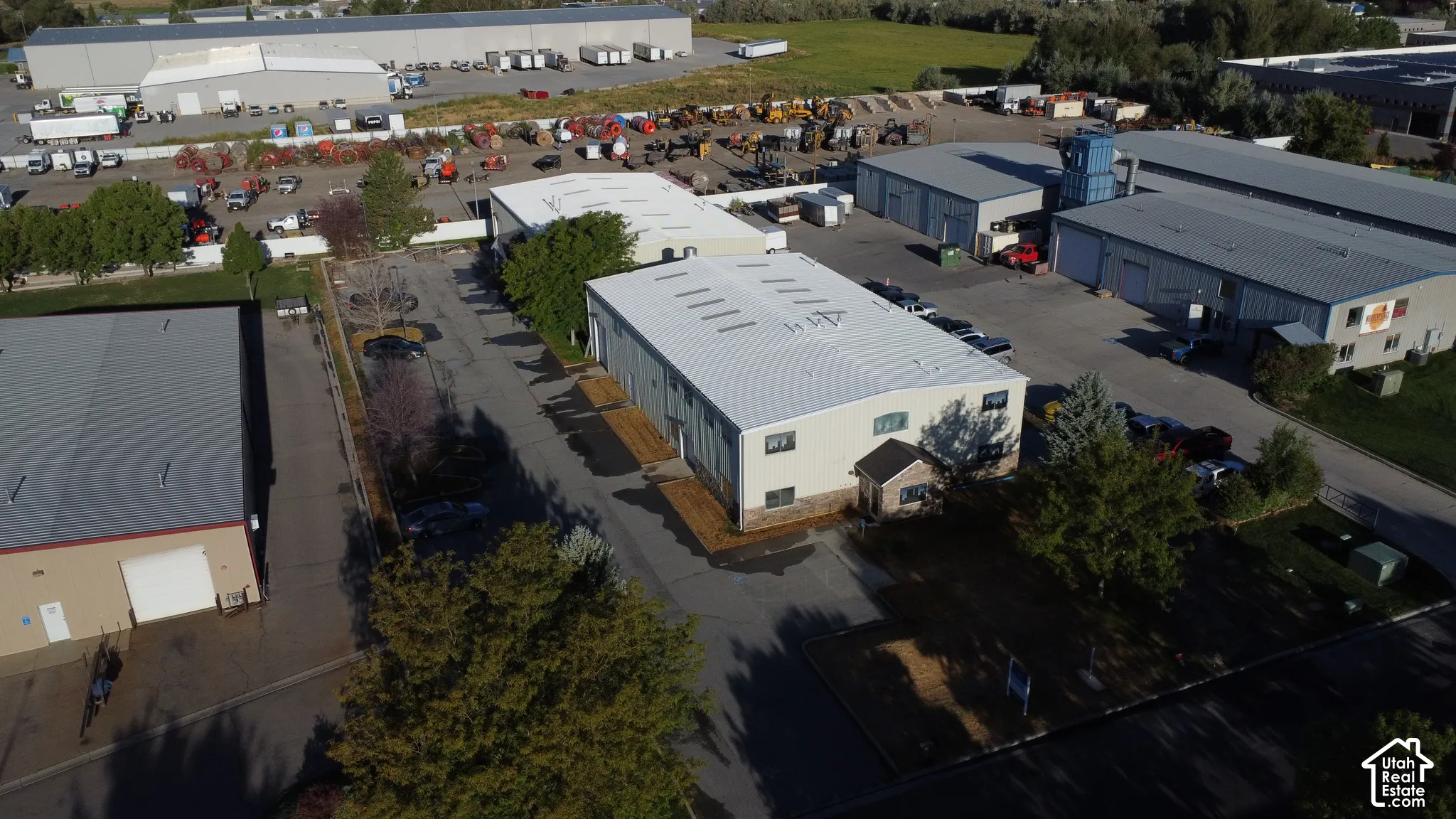 Commercial property featuring multiple industrial buildings with light-colored roofs, paved driveways, and surrounding green spaces