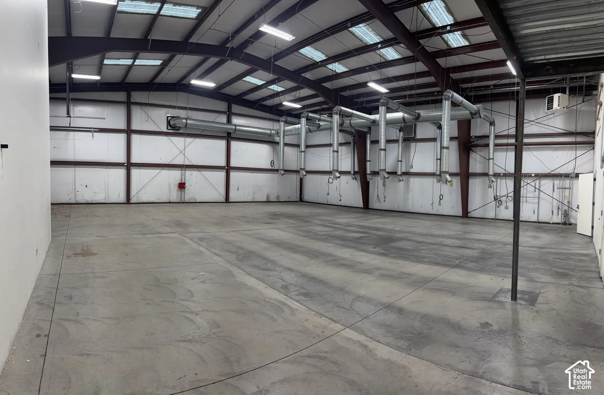 Expansive concrete flooring in a large open space, featuring multiple overhead lighting fixtures and extensive ceiling-mounted ductwork
