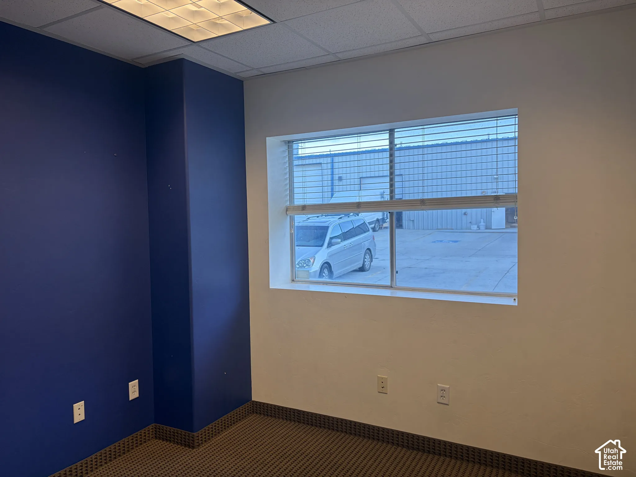 Recessed ceiling lighting, textured ceiling tiles, window with horizontal blinds, carpeted flooring, and a column accent