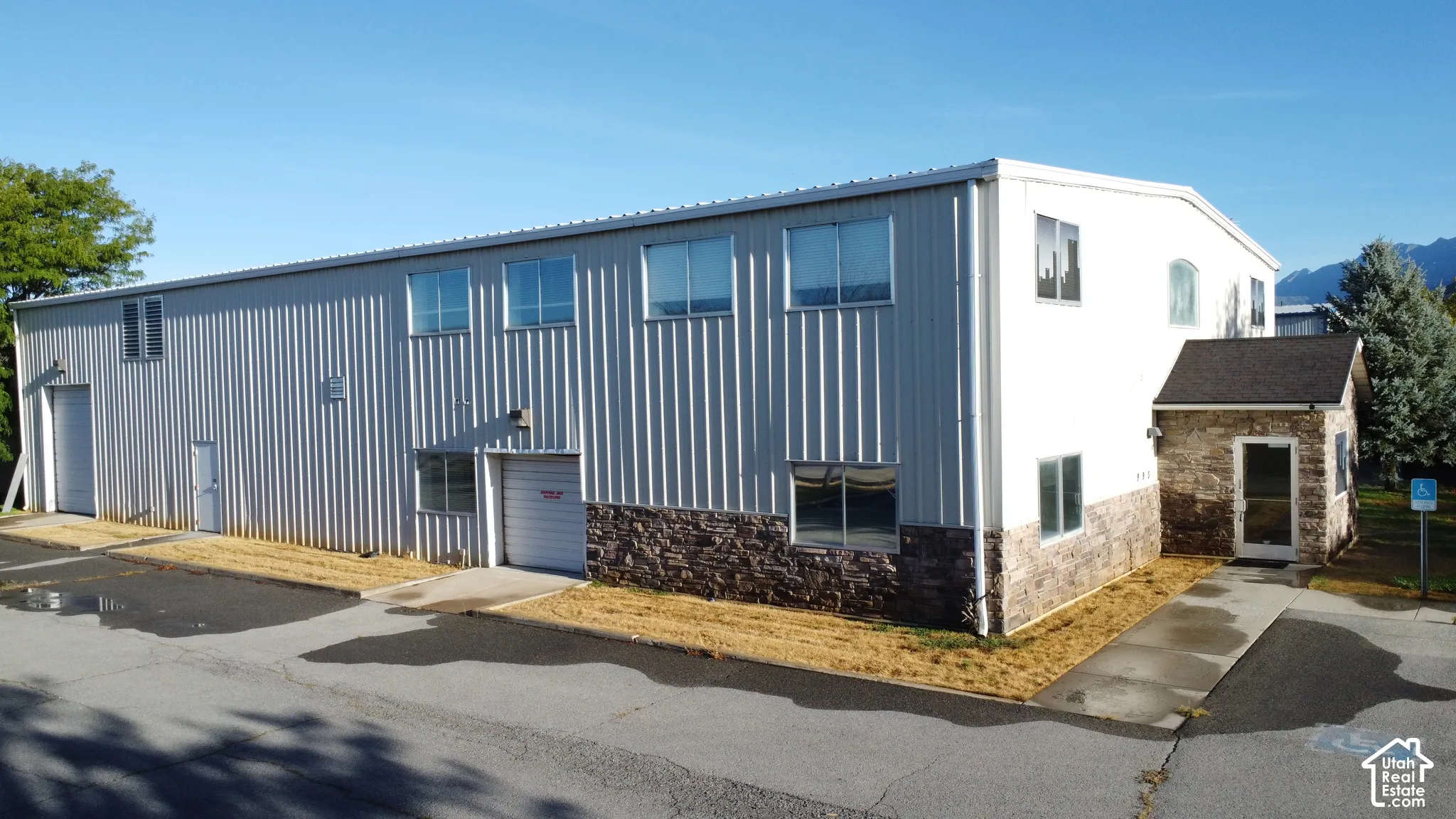 Industrial building with corrugated metal siding, partial stone veneer, multiple windows, and two roll-up doors