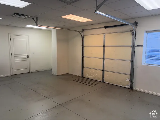 Concrete flooring, white painted walls, white panel door, fluorescent overhead lighting, and a window with horizontal blinds