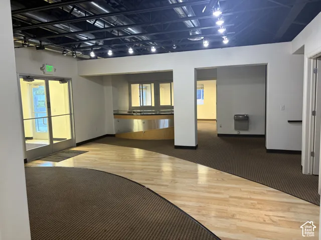 Exposed ceiling with track lighting, glass entry doors, built-in reception desk, wood-finish flooring, and wall-mounted water fountain