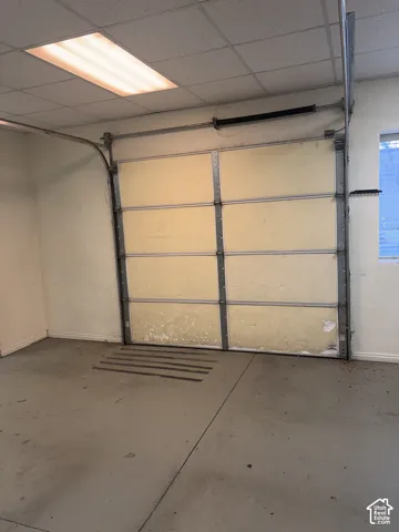 Sectional garage door with overhead track system, concrete flooring, and drop ceiling with recessed fluorescent lighting
