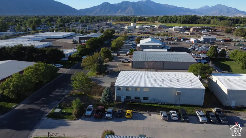 Industrial property featuring multiple buildings, expansive paved parking, and a backdrop of distant mountains