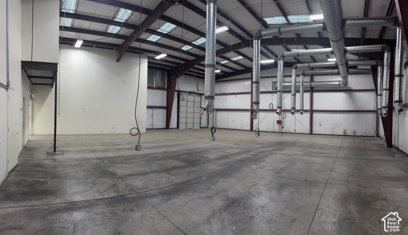 Expansive concrete flooring with high ceilings, featuring exposed metal trusses and extensive ductwork, complemented by multiple overhead skylights and bright overhead lighting