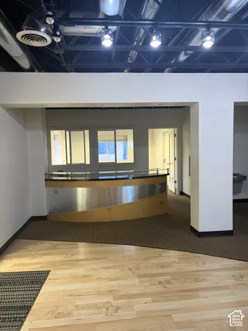 Hardwood flooring, exposed ceiling with ductwork and track lighting, curved reception desk with wood-finish and metal accents, interior windows, and a built-in water fountain
