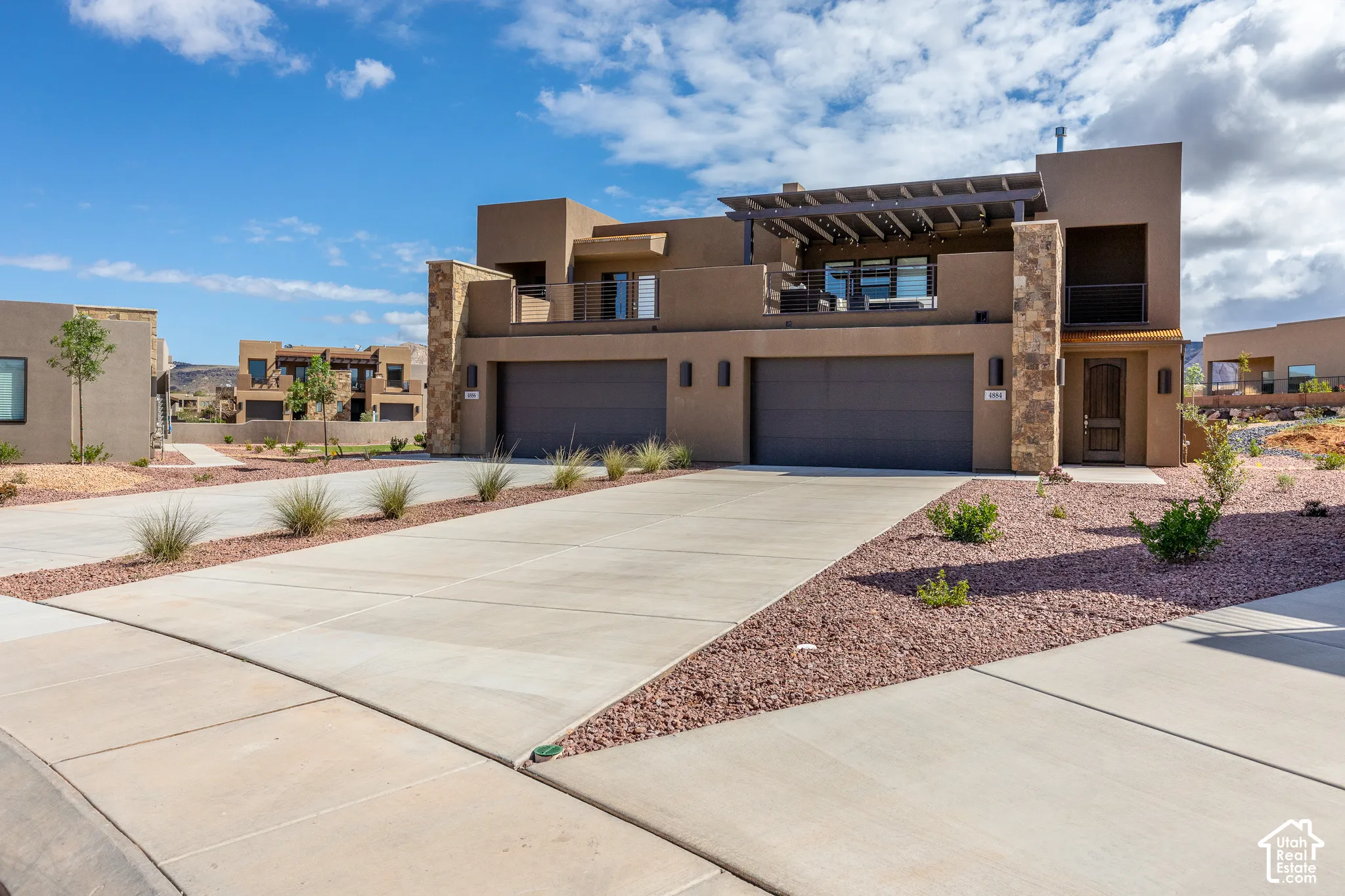 Contemporary stucco exterior with stone accents, an upper-level balcony with a pergola, and dual garage doors