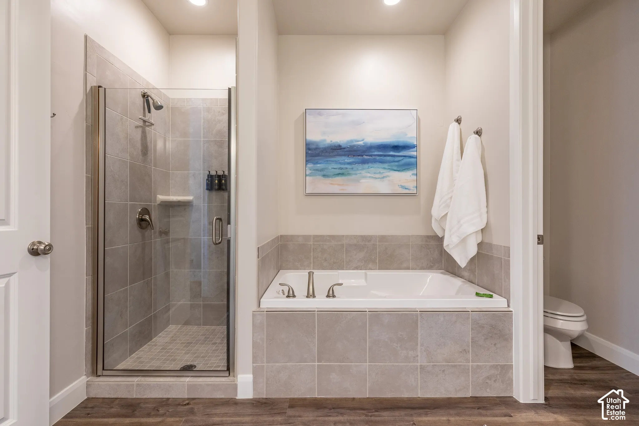 Tile-surround soaking tub with bronze-finish fixtures, a glass-enclosed shower with tile surround, and wood-finish flooring