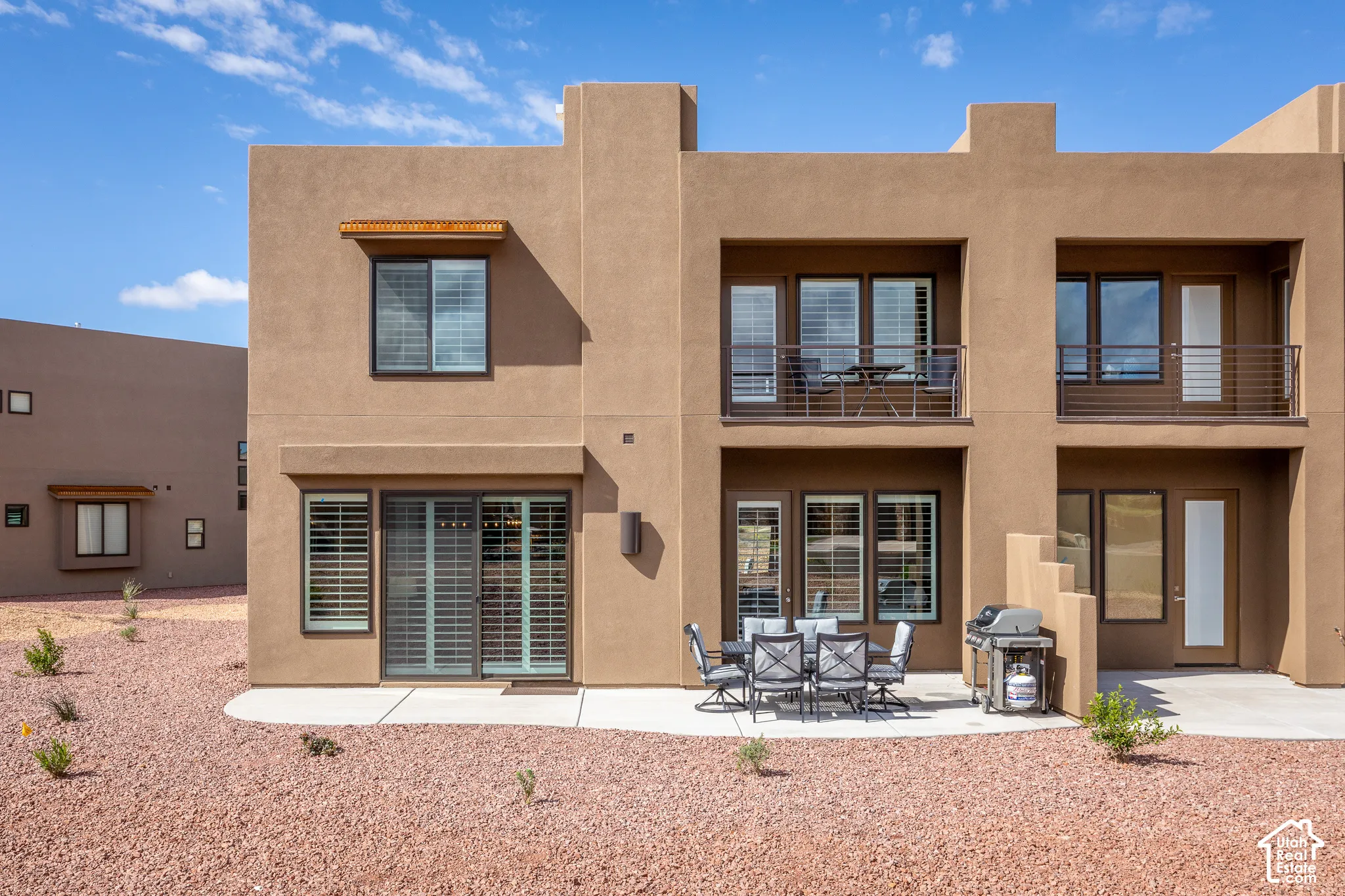 Stucco exterior with multiple balconies, ground-level patio, and sliding glass doors