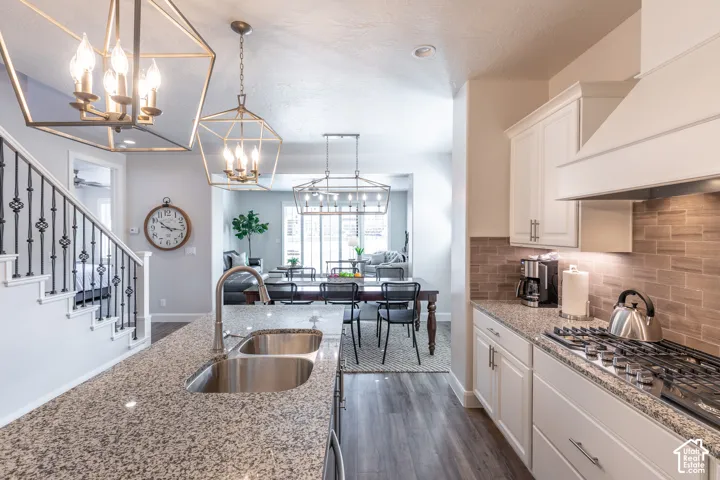 Granite countertops, dual stainless steel sink, wood-finish flooring, white cabinetry, and a gas range