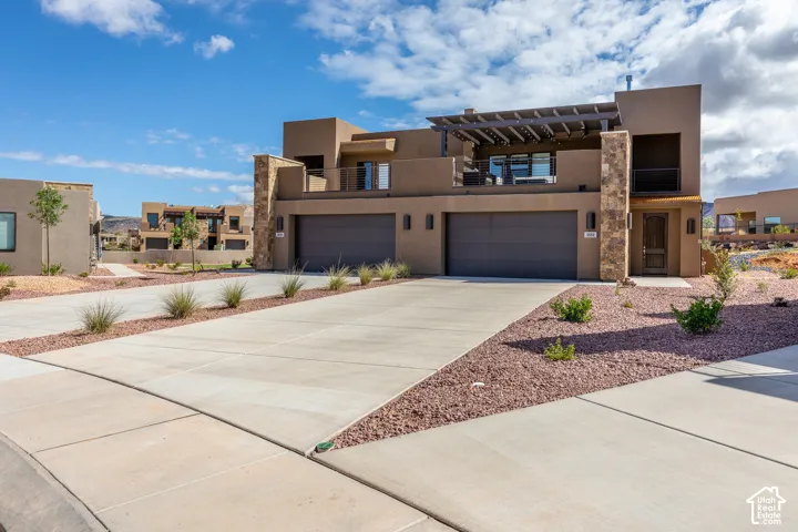 Contemporary stucco exterior with stone accents, an upper-level balcony with a pergola, and dual garage doors