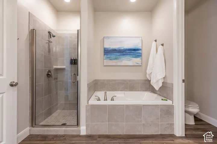 Tile-surround soaking tub with bronze-finish fixtures, a glass-enclosed shower with tile surround, and wood-finish flooring
