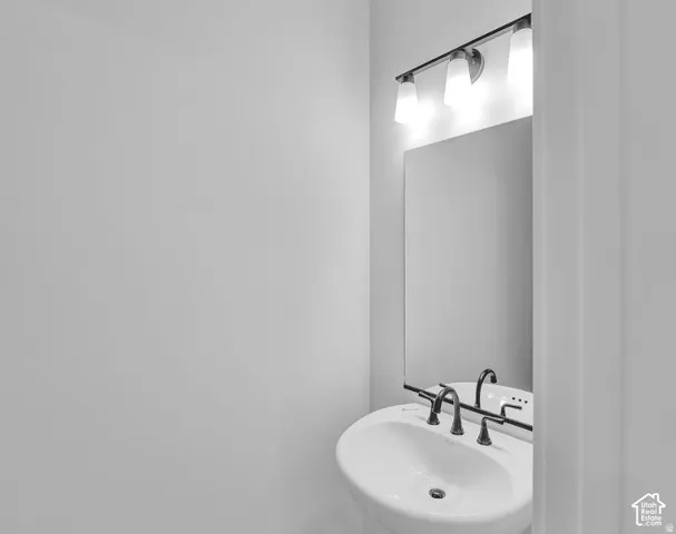 Pedestal sink with a three-piece faucet, rectangular wall mirror, and a three-light vanity fixture
