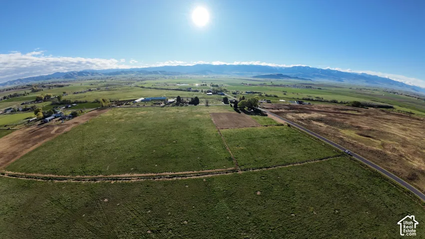 Expansive green fields, distant mountains, clear blue sky, and a paved road