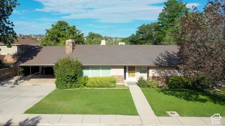 Ranch-style residence featuring a brown shingle roof, stone-clad chimney, and a covered carport