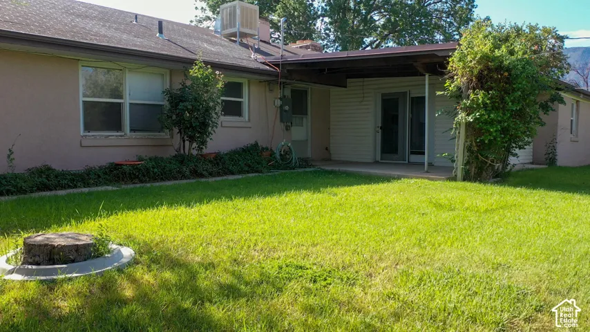 Expansive grassy yard with a covered patio, multiple windows, and exterior stucco finish