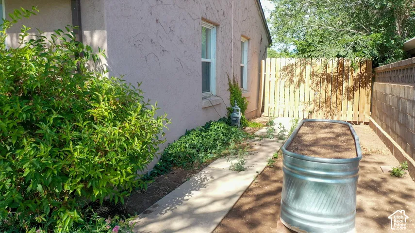 Exterior featuring stucco siding, multiple windows, a concrete pathway, and a wooden privacy fence