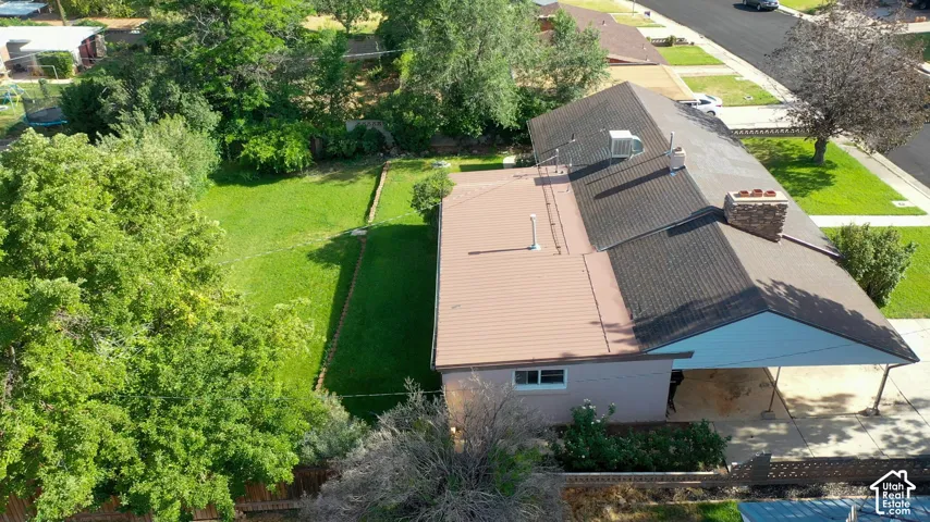 Expansive rear yard with manicured lawn, established landscaping, attached carport, and a stone chimney