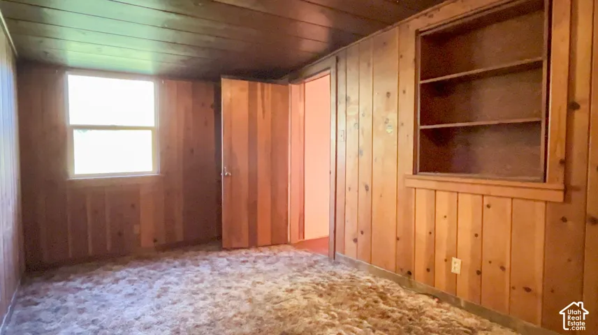 Wood-paneled room featuring a built-in shelving unit, a window, and a wood-paneled door