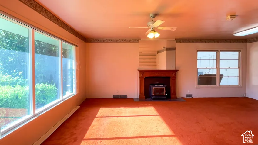 Expansive picture windows, wood-finish mantel, wood-burning stove, ceiling fan, and wall-mounted lighting